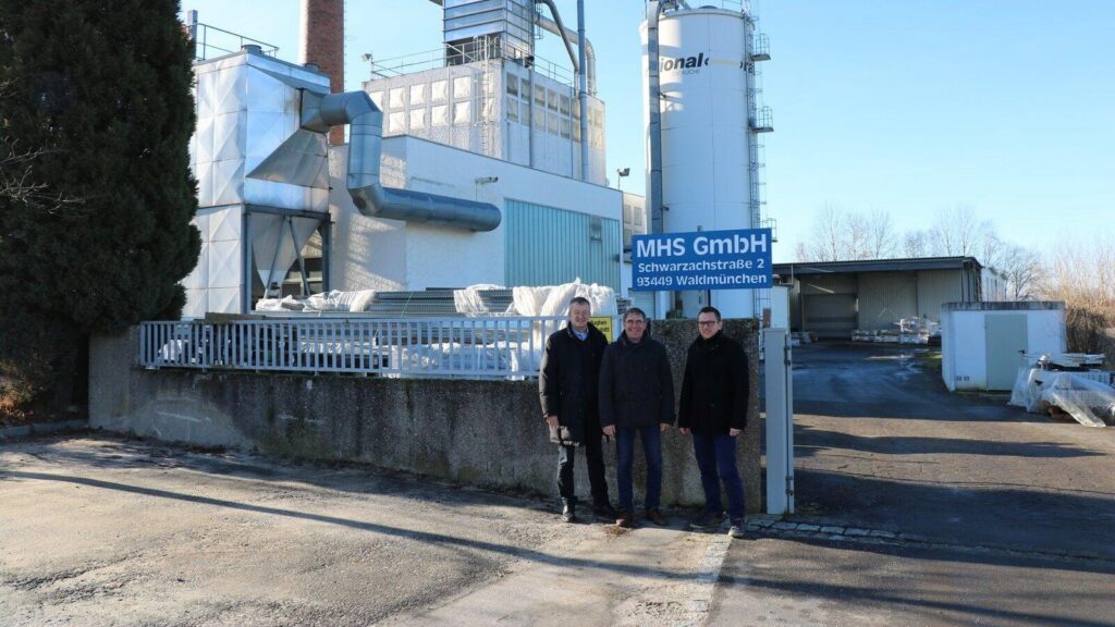 Bürgermeister Markus Ackermann (links) steht gemeinsam mit den Geschäftsführern Johann und Mathias Schießl vor dem Werkstor und dem blauen Firmenschild der MHS GmbH in Waldmünchen.