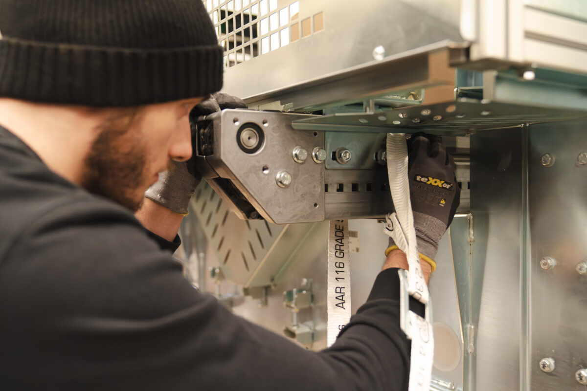Ein Mitarbeiter der MHS GmbH sichert ein Industriegut mit Spanngurten im Verpackungsprozess.