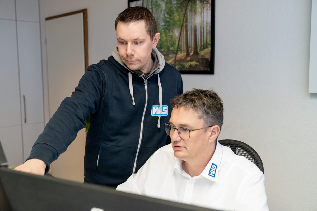 Geschäftsführer Mathias Schießl bespricht Details einer Metallkonstruktion mit einer Mitarbeiterin, die Daten auf einem Tablet erfasst.