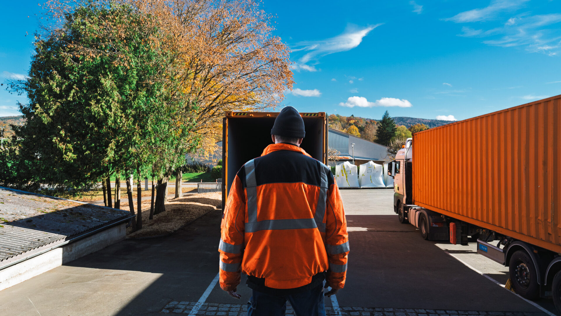 Mitarbeiter in Warnjacke steht vor einem geöffneten LKW-Container auf dem MHS Logistikgelände.