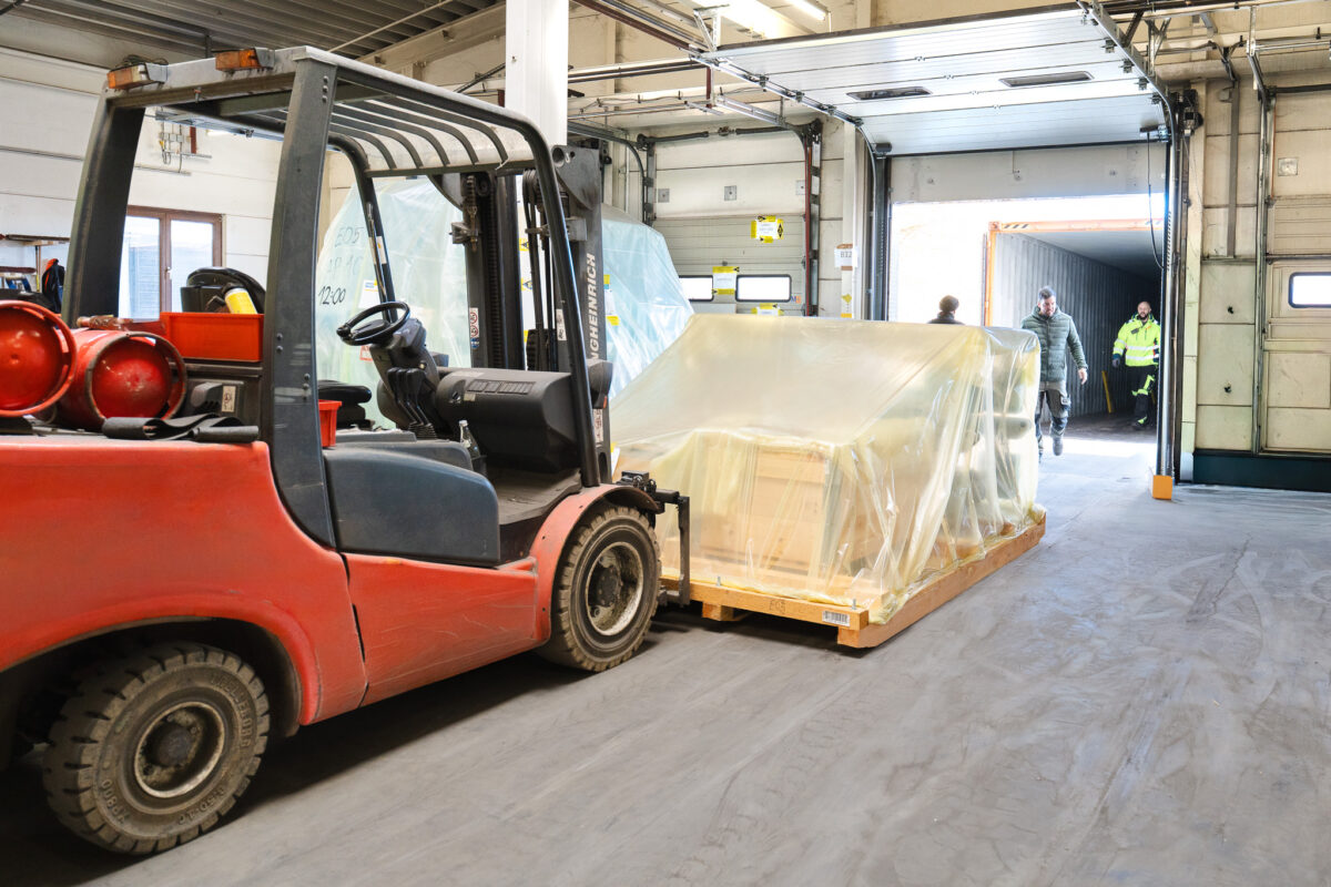 Roter Gabelstapler fährt foliertes Frachtstück zur Containerstauung in einen Seecontainer.