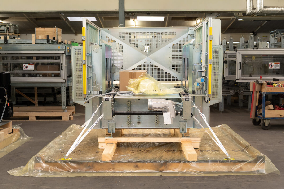 Transportsichere Verpackung einer großen Industriemaschine auf einer Holzkonstruktion, gesichert mit weißen Zurrgurten und Schutzfolie durch die MHS GmbH.