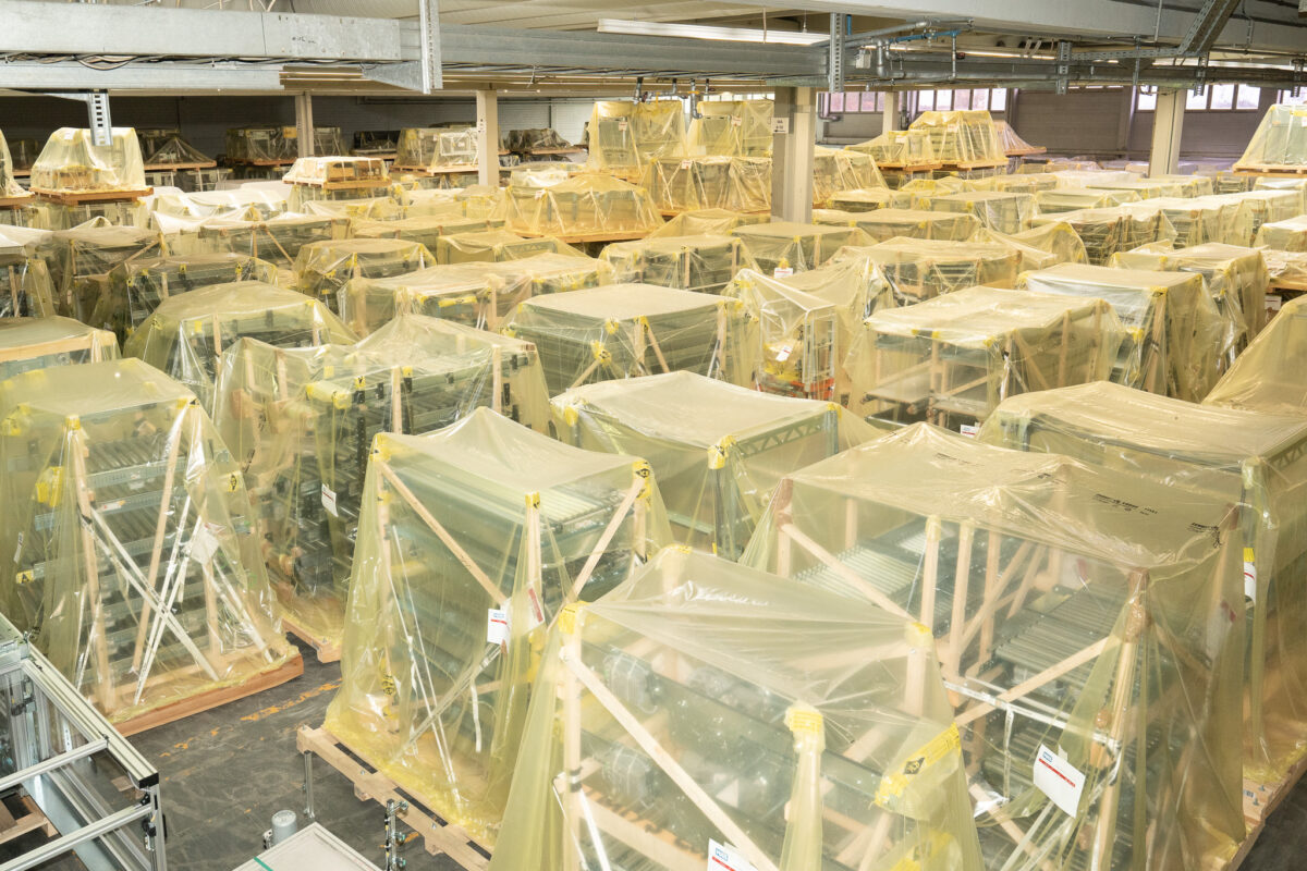 Blick in eine voll belegte Lagerhalle der MHS GmbH. Zahlreiche in Schutzfolie verpackte Industriemaschinen stehen witterungsgeschützt zur Einlagerung bereit.