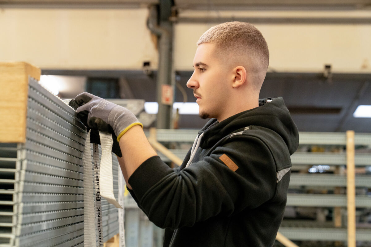 Ein Mitarbeiter der MHS GmbH sichert Metallbauteile mit Gurten. Symbolbild für die praktische Umsetzung im Logistic Management.