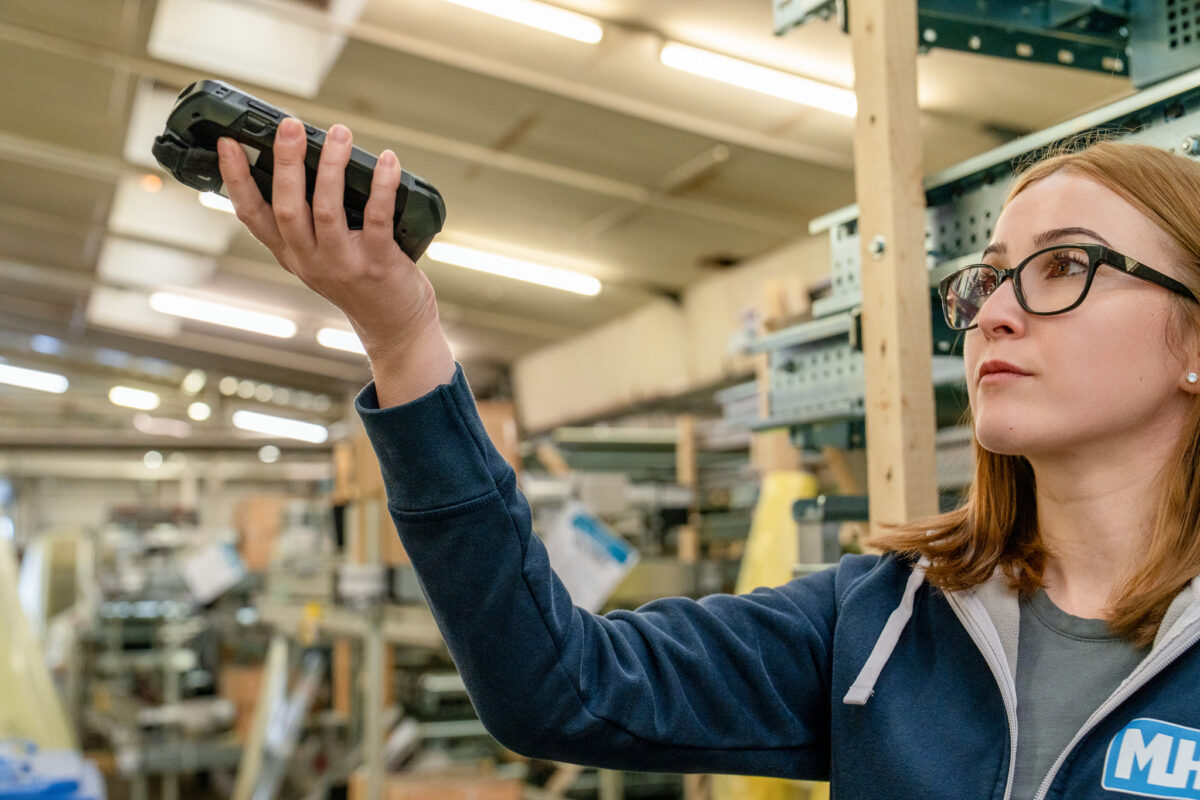 Eine Mitarbeiterin der MHS GmbH erfasst Lagerbestände mit einem digitalen Handscanner. Symbolbild für effiziente Supply Chain Prozesse und Warenstrom-Optimierung.