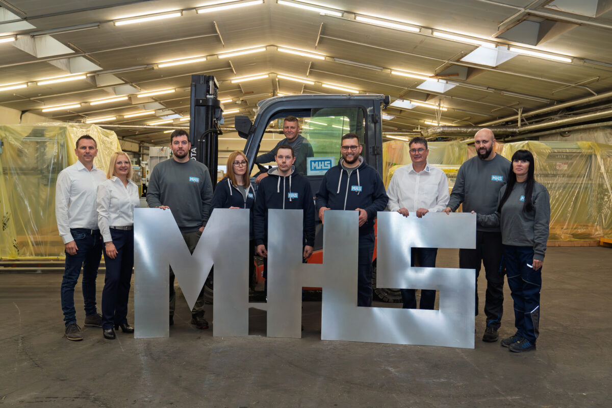 Das Team der MHS GmbH in Waldmünchen. Mitarbeiter und Geschäftsführung halten gemeinsam große silberne Metallbuchstaben "MHS".